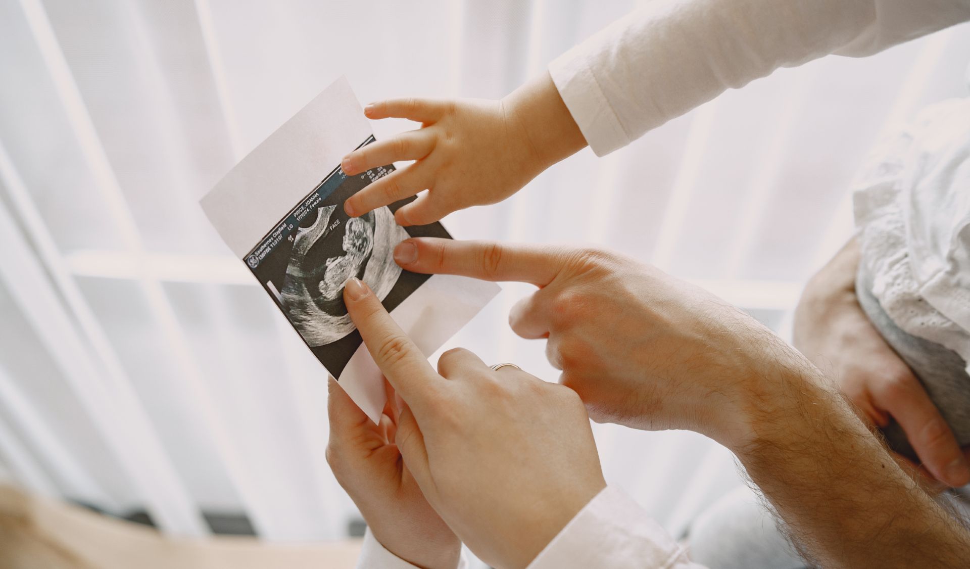 mom dad daughter watching ultrasound picture baby family light clothes family expecting baby